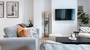 Un salon moderne avec un canapé gris, une table basse noire et un téléviseur à écran plat fixé au mur.