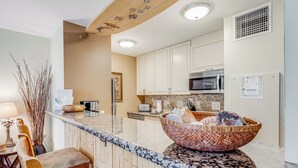 A kitchen with a granite countertop, white cabinets, a microwave, and a large woven bowl on the island.