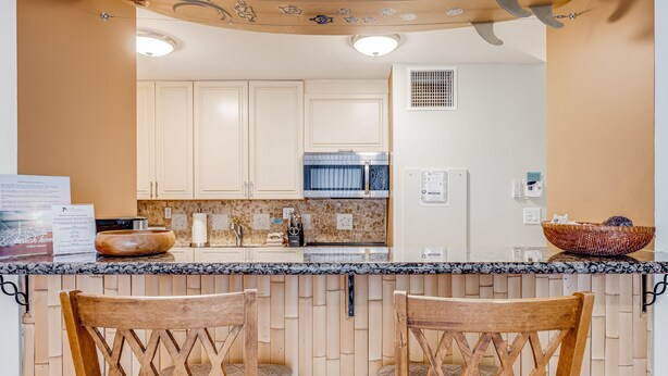 A kitchen with wooden cabinets, a granite countertop, and a bar area with two wooden chairs.