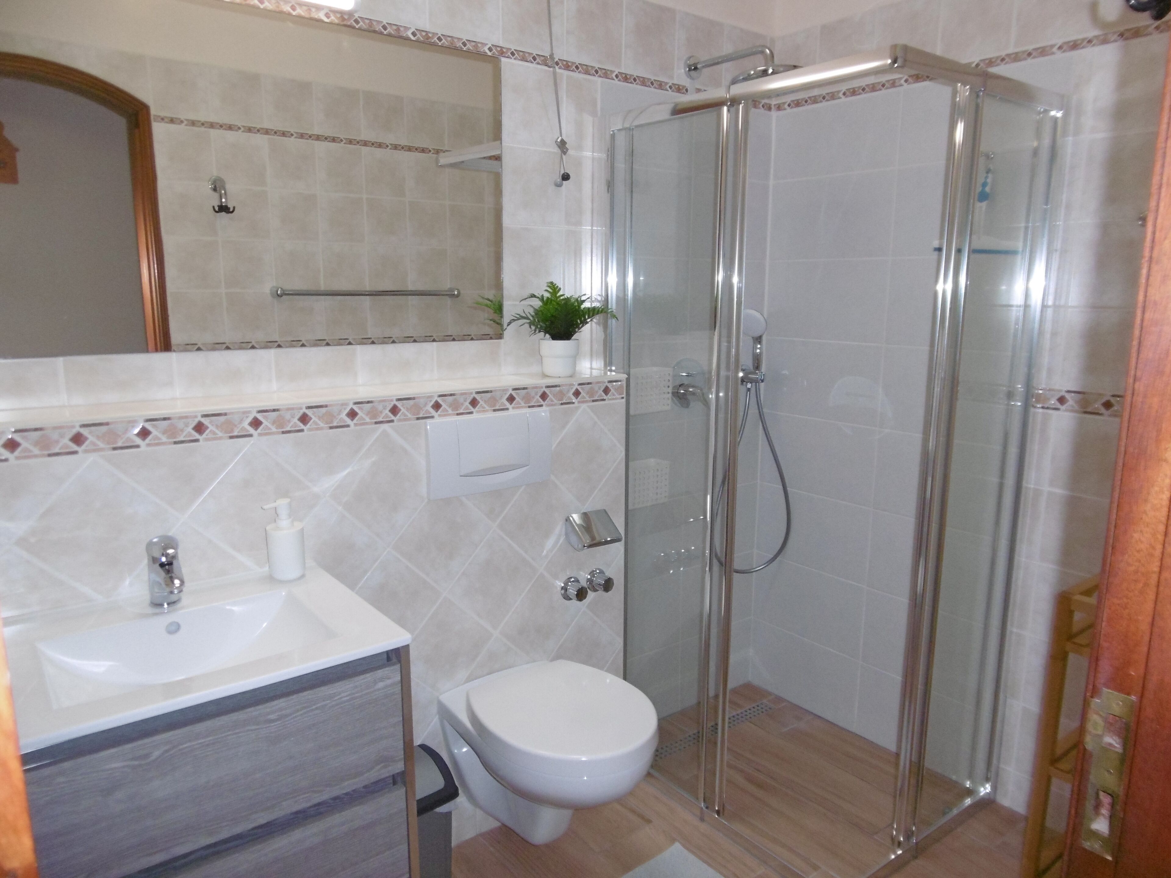Uma casa de banho moderna com chuveiro de vidro, sanita branca e lavatório com espelho em cima.