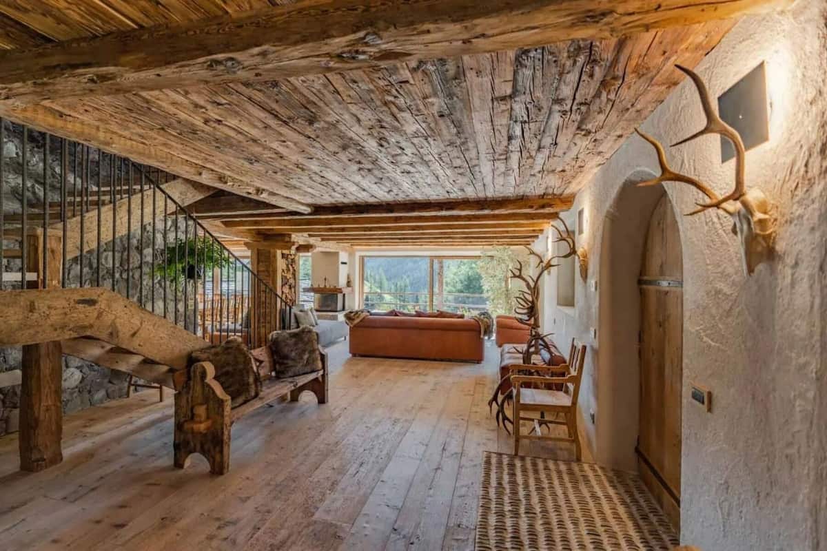 Un interior rústico con vigas de madera a la vista, una escalera de piedra, un sofá y decoración de cornamentas.