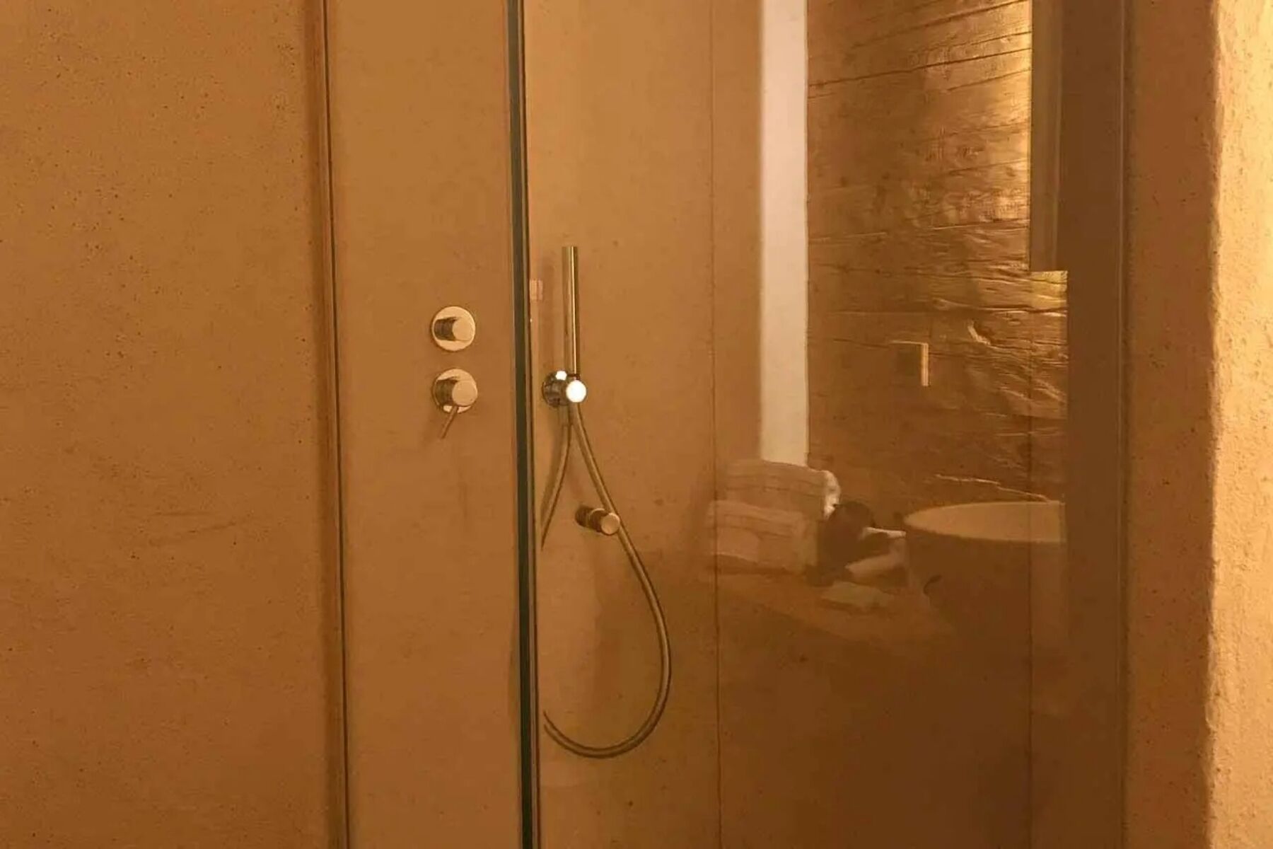 Eine gläserne Duschkabine mit freistehendem Waschtisch und einer Wand aus Stein im Hintergrund.