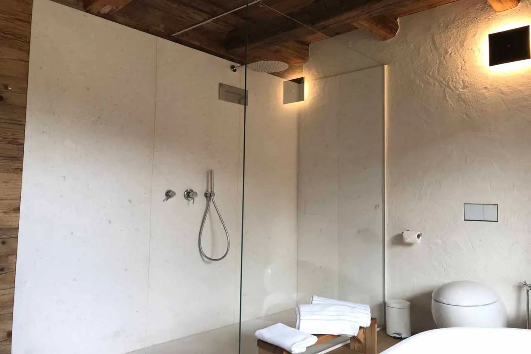 Un baño moderno con cabina de ducha de vidrio, techo de madera y lavamanos blanco.