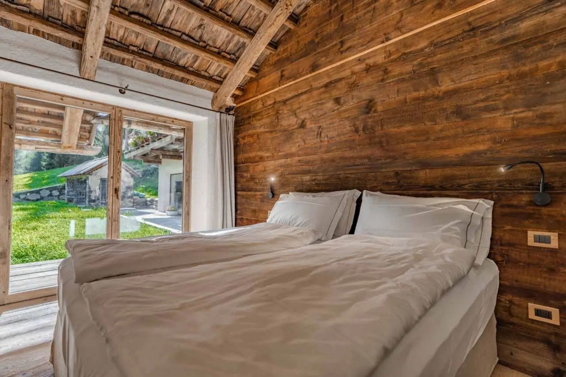 A wooden room with a bed, a window, and a view of greenery.