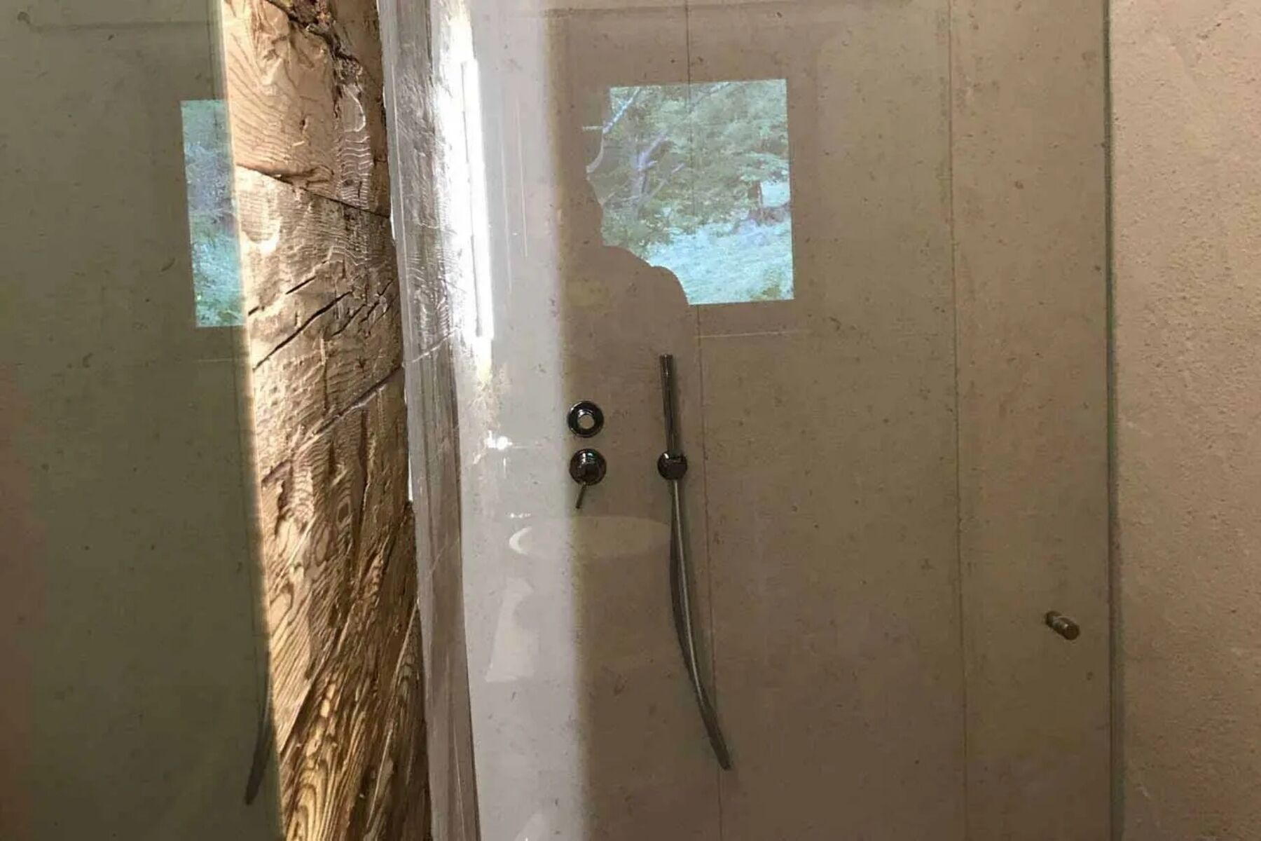 Ein Badezimmer mit Holztür, Dusche und Blick auf einen Wald durch ein Fenster.