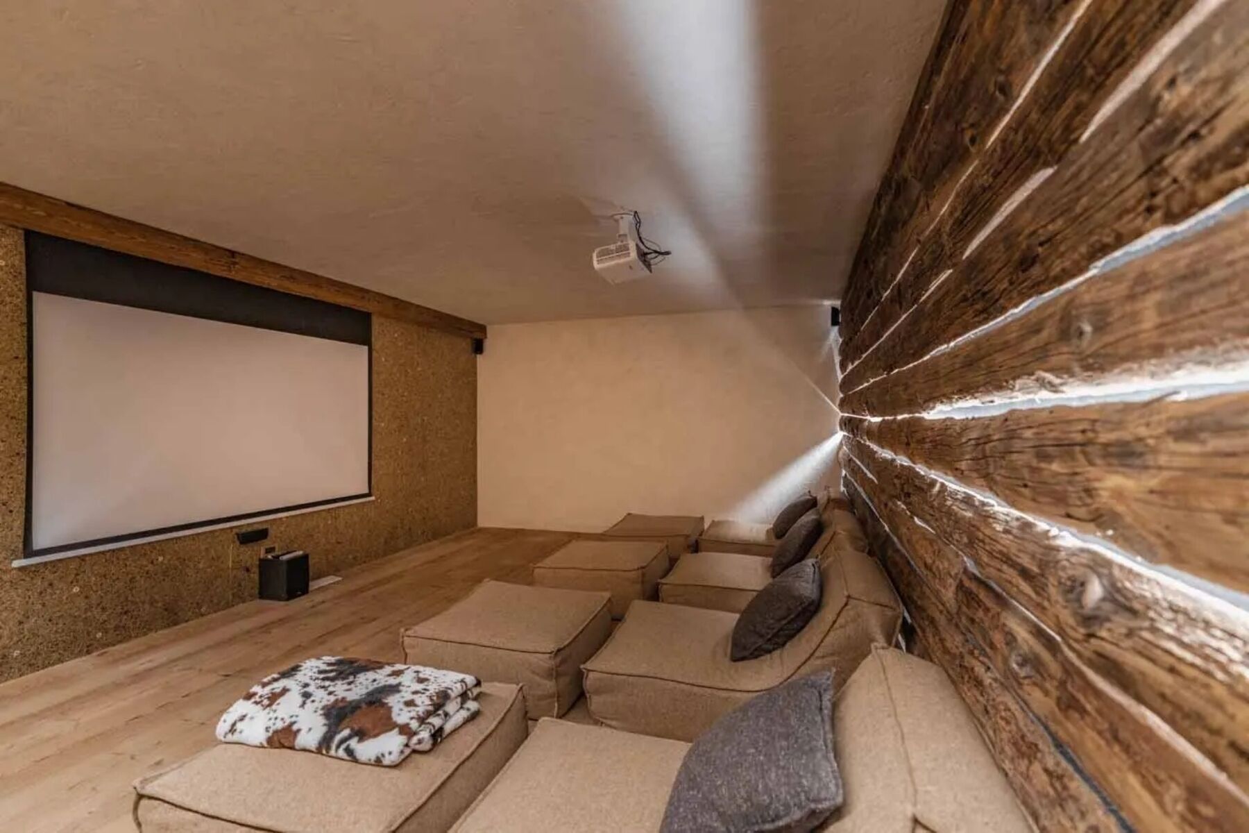 Une pièce chaleureuse équipée d’un écran de projection, de lambris en bois et d’un canapé agrémenté de coussins.