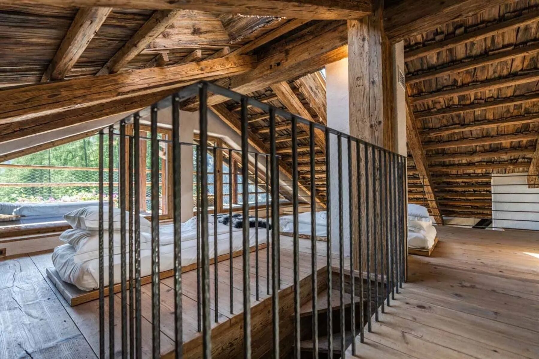Un dormitorio tipo loft con techo de madera, escalera de metal y vistas al exterior.