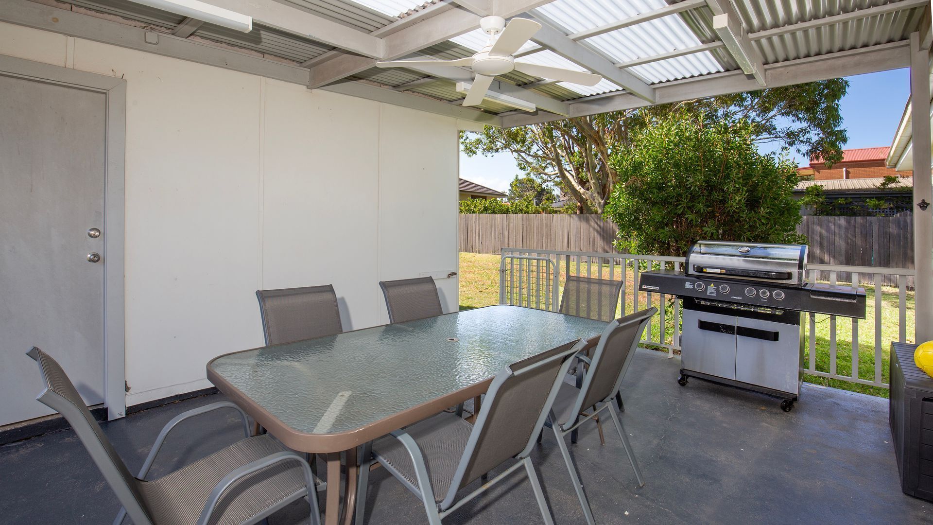 Een overdekt terras met een tafel, stoelen, een barbecue en een deur.