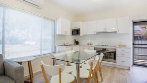 A modern kitchen with white cabinets, a glass dining table, and a grey sofa.