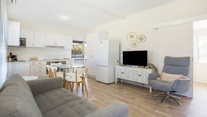 A modern kitchen with white cabinets, a dining table with chairs, a grey sofa, and a grey armchair.