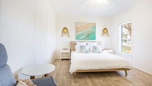 A bedroom with a bed, bedside tables, a chair, a small table, and a window.