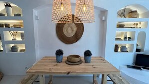 Una mesa de madera para comer con bancos, dos lámparas colgantes y un espejo redondo sujeto a la pared.