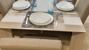 Une table à manger dressée pour six personnes, avec de l’argenterie blanche, de la verrerie bleue et un petit modèle de bateau décoratif.