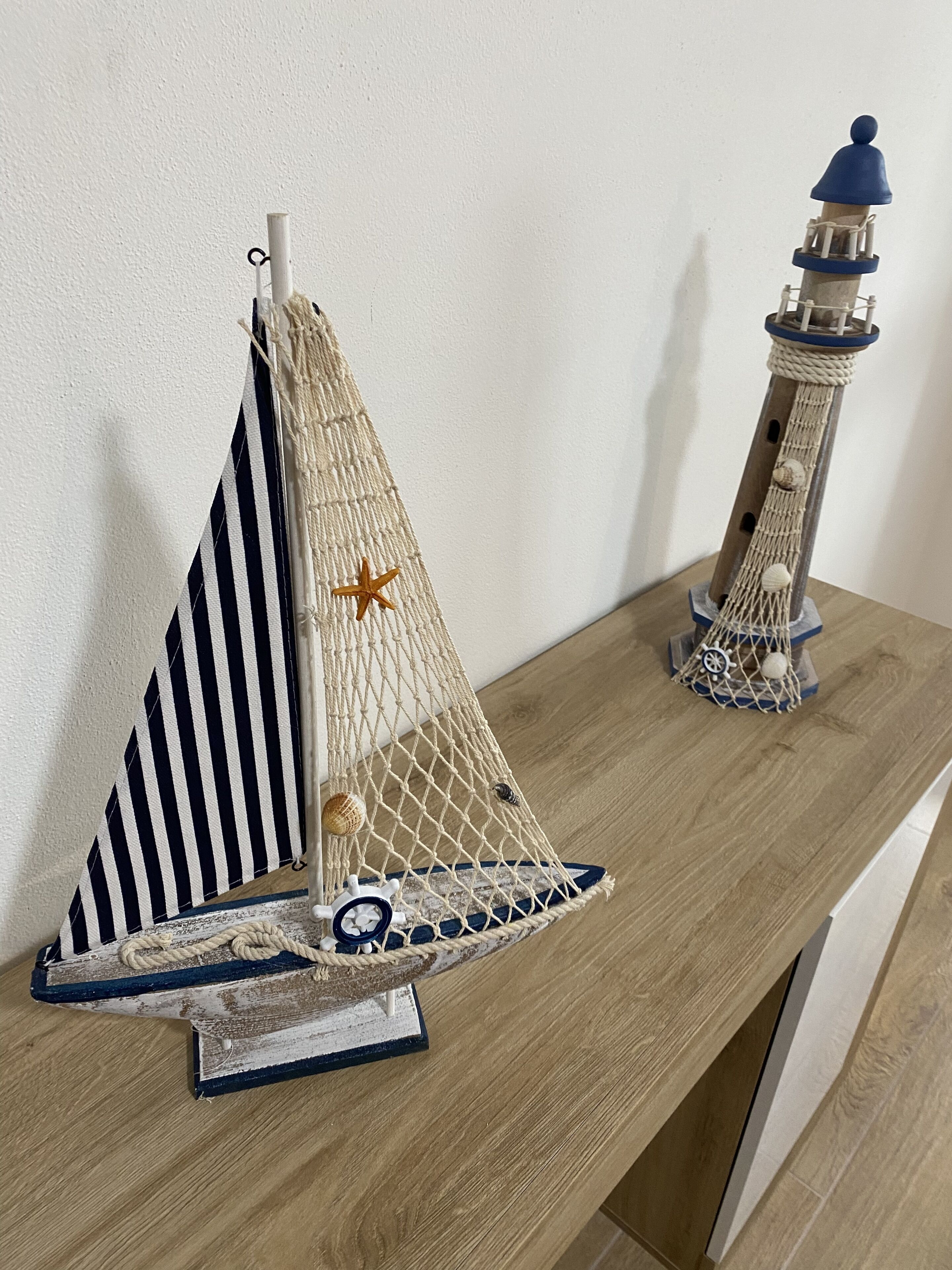 A wooden shelf with two nautical-themed decorative items: a sailboat and a lighthouse model.