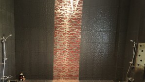 Ein modernes Badezimmer mit dunklen Wänden, einer zentral platzierten Mosaikfliesenwand und einer Duschkabine mit einer Glaskonstruktion.