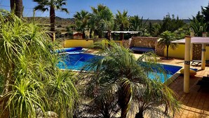 A swimming pool surrounded by palm trees and a stone wall. - Bungalow with apartment in a quiet location and large pool (Burgau)