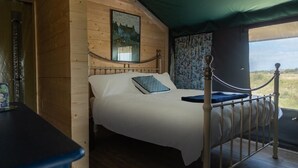 A wooden cabin room with a bed, a framed picture on the wall, and a view through a window.