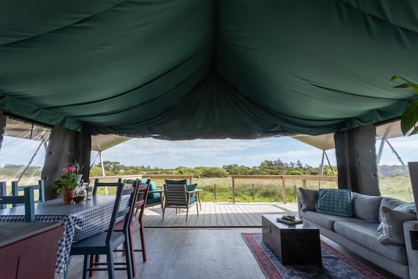 A tented outdoor area with a dining table, chairs, and a sofa.