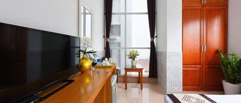 A hotel room with a flat-screen TV, wooden desk, potted plants, and a large wardrobe.