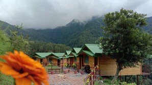 A row of wooden cabins with green roofs, surrounded by lush greenery and mountains in the background. - LaSerene The Cottage (Nainital)