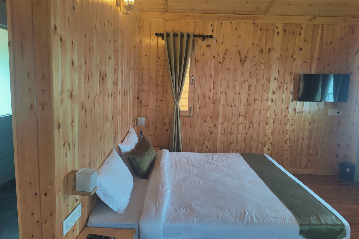 A wooden room with a bed, a TV mounted on the wall, and a window with curtains.
