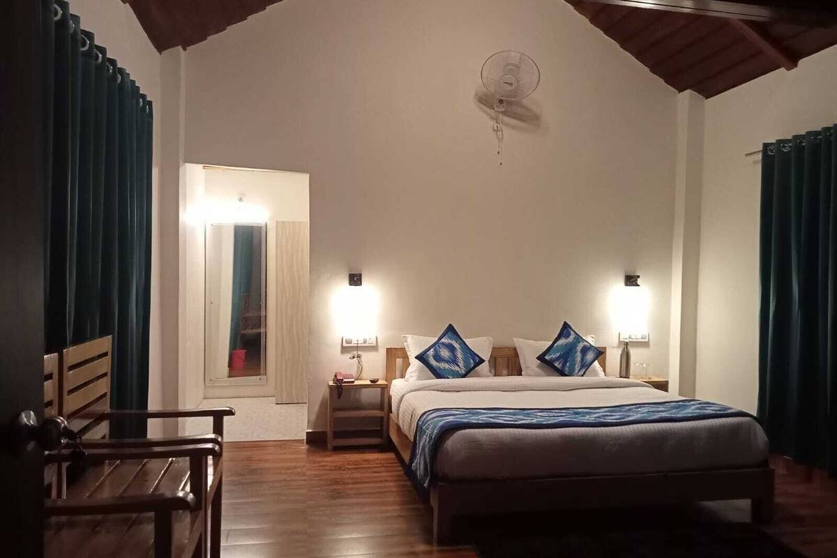 Ein Schlafzimmer mit einem Bett, Nachttischlampen, einem Ventilator, einer Holzbank und einer Tür zu einem anderen Raum.