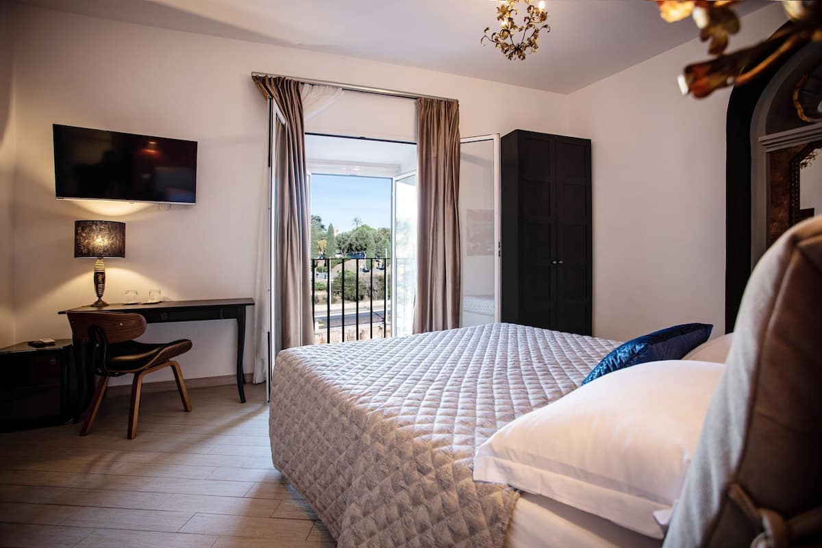 A bedroom with a bed, a desk, a chair, a TV, and a balcony.
