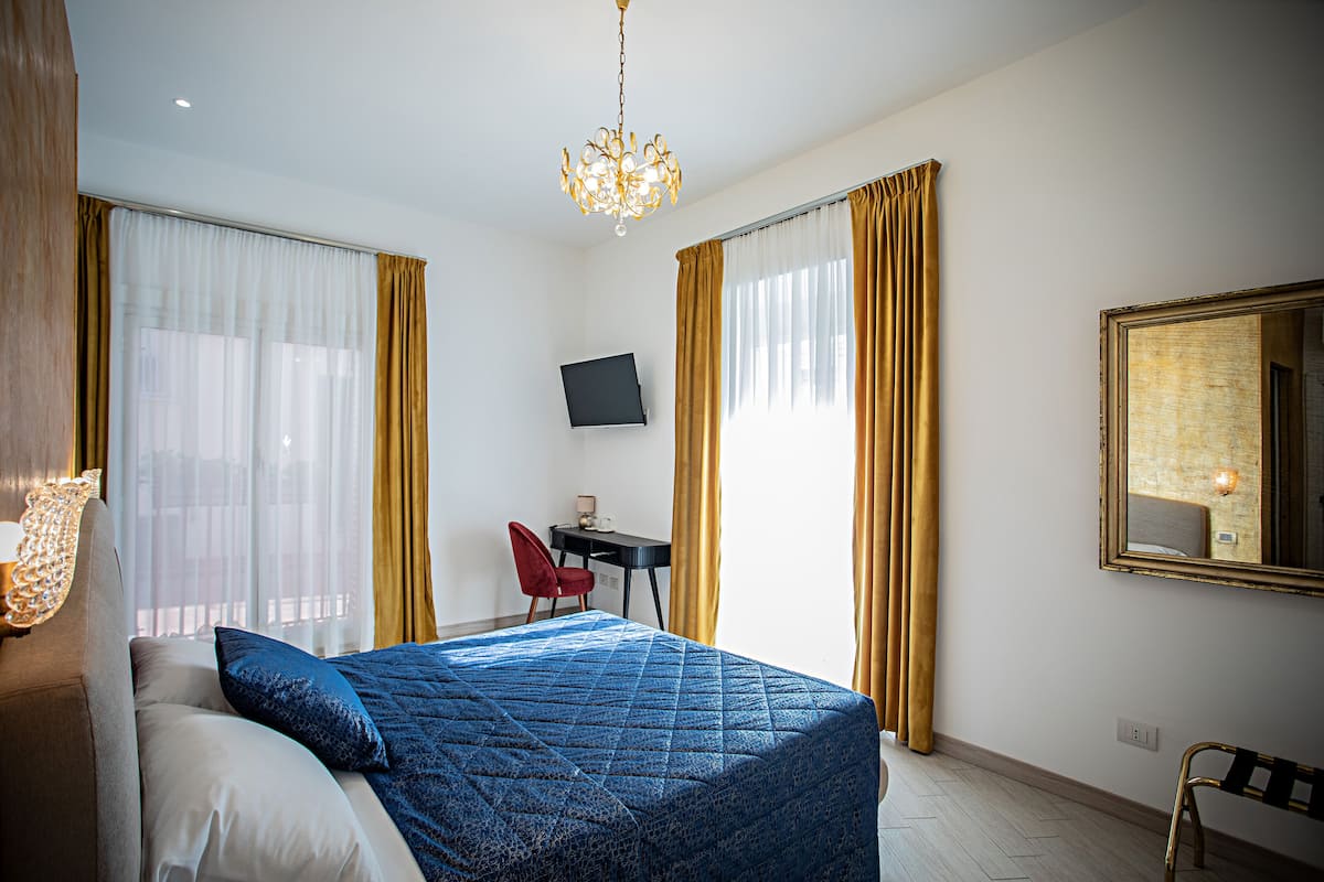A hotel room with a bed, a desk, a chair, a TV, and a large mirror.