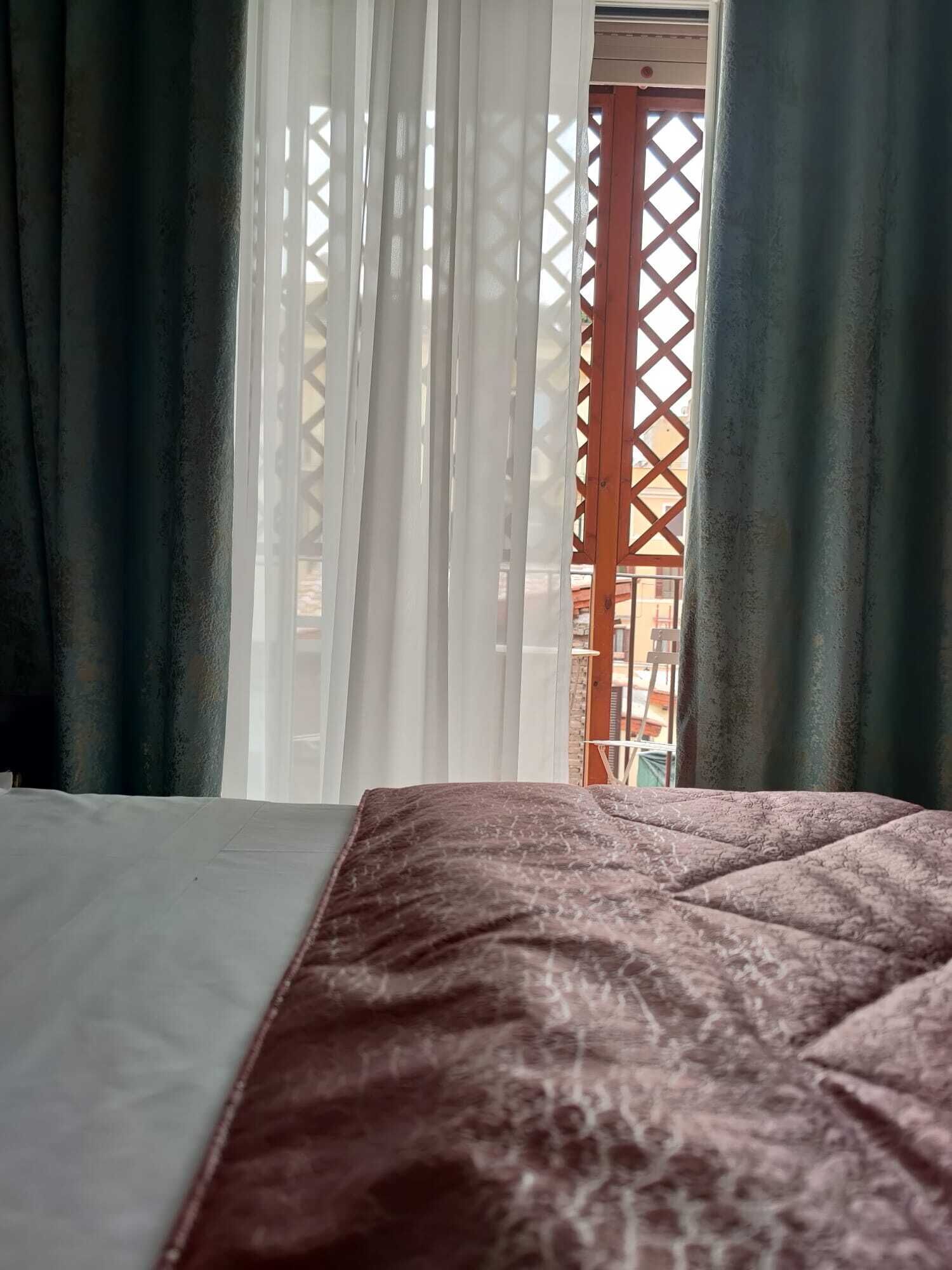 A bed with a patterned bedspread, sheer curtains, and a view through a lattice window.