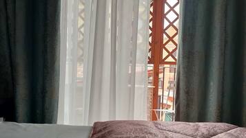A bed with a patterned bedspread, sheer curtains, and a view through a lattice window.