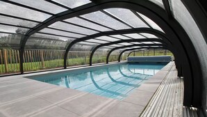 Ein überdachter Pool mit Glasdach, umgeben von einer Holzterrasse.