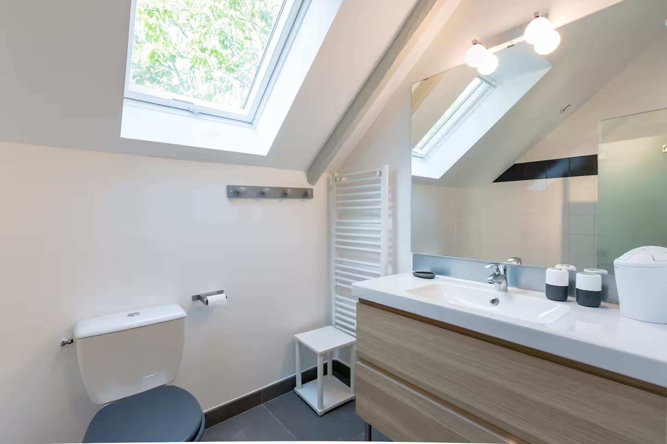 Une salle de bain moderne avec des fenêtres de toit, un lavabo blanc et un miroir.