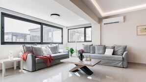 A modern living room with two grey sofas, a wooden coffee table, and large windows offering a view of buildings. - Liberty's Canvas - Balcony Suite near Acropolis (Αθήνα)