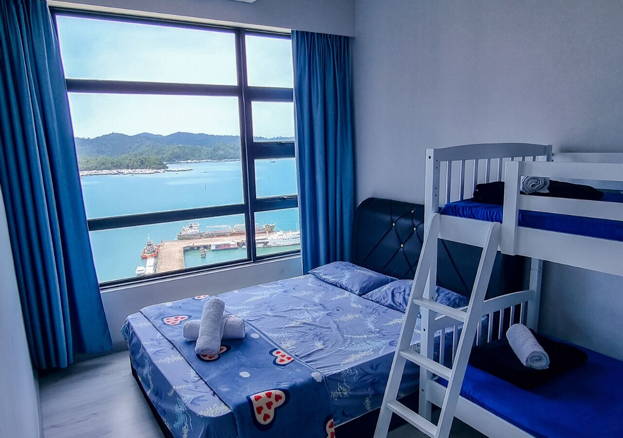 Une chambre avec un lit superposé, une grande fenêtre donnant sur la mer et une île lointaine, et un lit recouvert d’une couvre-lit à motifs bleus et blancs.