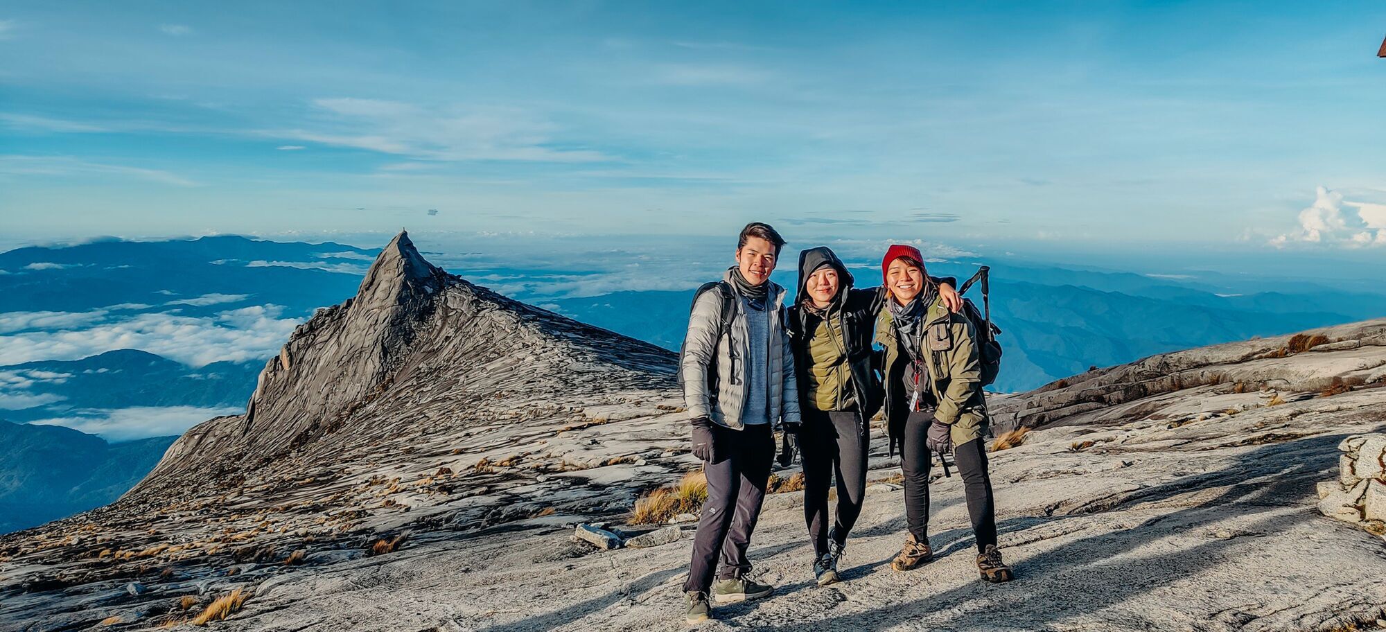 A group of people on a rocky mountain trail with a clear sky and distant mountains.