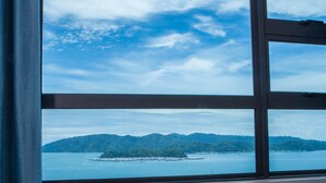 A window with a view of a body of water and a distant landmass. - Jesselton Point Homestay  (Kota Kinabalu)