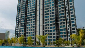 A tall hotel with a swimming pool in front, surrounded by palm trees. - Jesselton Point Homestay  (Kota Kinabalu)