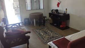 A small, well-lit room with a bed, a desk with a chair, a small table with two chairs, a rug, and a window with blinds. - Simple and spacious house for Carnival. (Mongaguá)