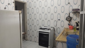 A kitchen with a white refrigerator, a gas stove, and a blue water container. - Simple and spacious house for Carnival. (Mongaguá)