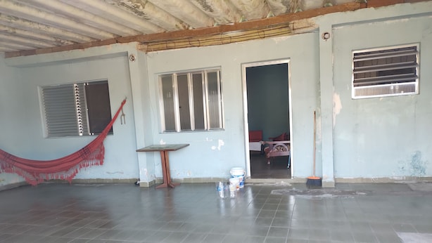 A room with a tiled floor, a hammock, a table, and a door leading to another room. - Simple and spacious house for Carnival. (Mongaguá)