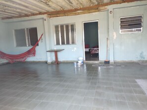 Una habitación con suelo de baldosas, una hamaca, una mesa y una puerta que da a otra estancia.