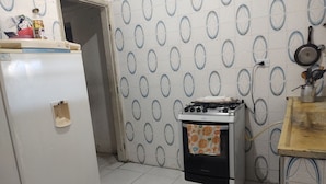 A kitchen with a refrigerator, stove, and tiled backsplash. - Simple and spacious house for Carnival. (Mongaguá)