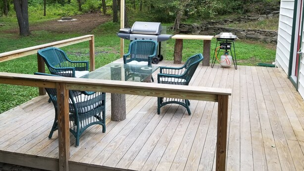 Eine Terrasse im Freien mit einem Tisch aus Glas, Korbstühlen, einem Grill und Lichterketten.