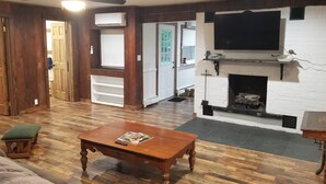 Ein Wohnzimmer mit Holzboden, Kamin, Wand-Fernseher und Deckenventilator.
