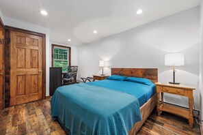Een slaapkamer met een bed, twee nachtkastjes, een nachtkastje, een houten garderobe en een raam met uitzicht op groen.