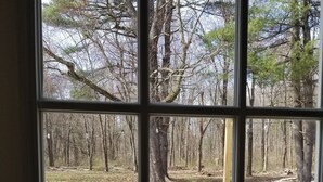 Blick durch ein Fenster auf einen Deckbereich mit Grill, Holztisch und einem Fahrrad.
