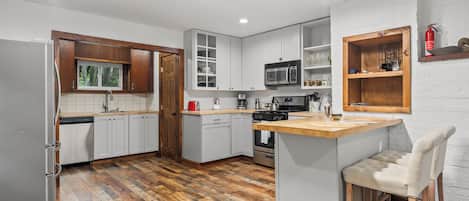 Una cocina moderna con armarios blancos, encimera de madera y una barra con un taburete.