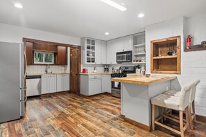 A modern kitchen with white cabinets, a wooden countertop, and a bar area with a stool. - The Calf Pen (Staatsburg)