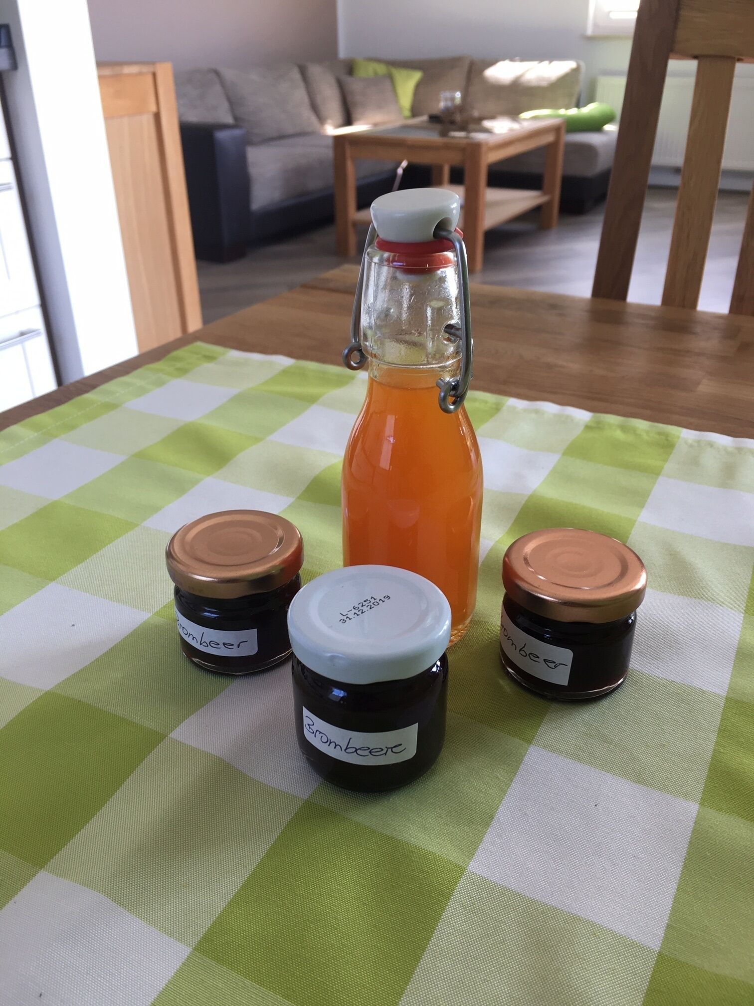 A table with a green and white checkered tablecloth, a glass bottle with a metal cap, and three small jars with metal lids.