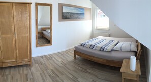 Quarto com guarda-roupa de madeira, cama com roupa de cama listrada, mesa de cabeceira de madeira e um quadro na parede.